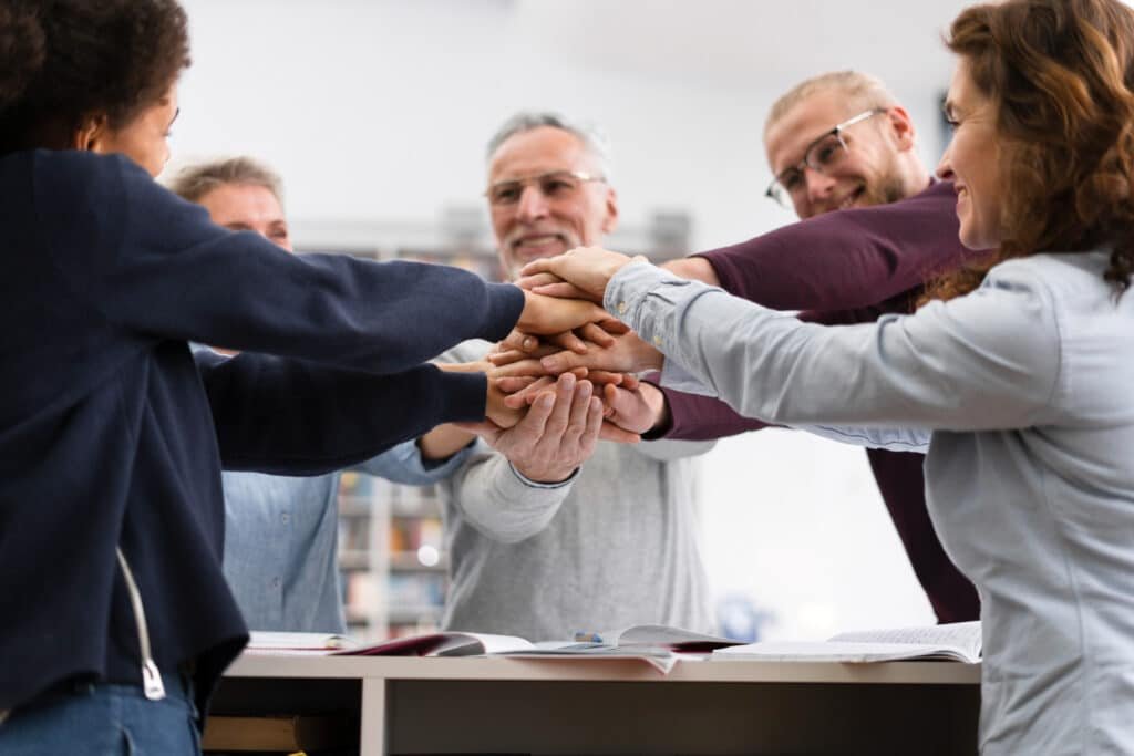 Réunion de team building avec un groupe de personnes souriant et se tenant par les bras.